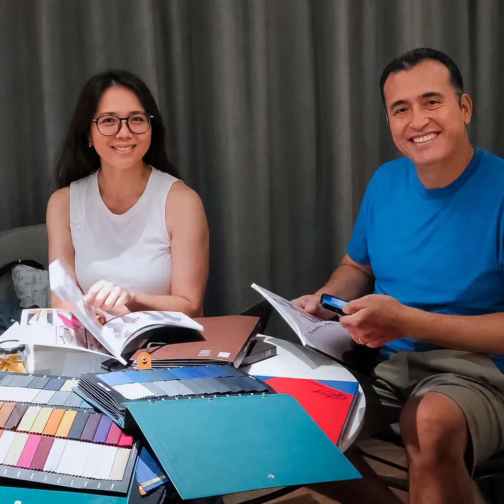 Two customers smiling at a table covered with fabric swatch books and cloth samples
