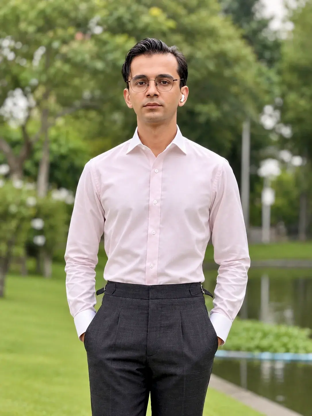 Man in a tailored light pink shirt and high-waisted grey trousers standing in a park