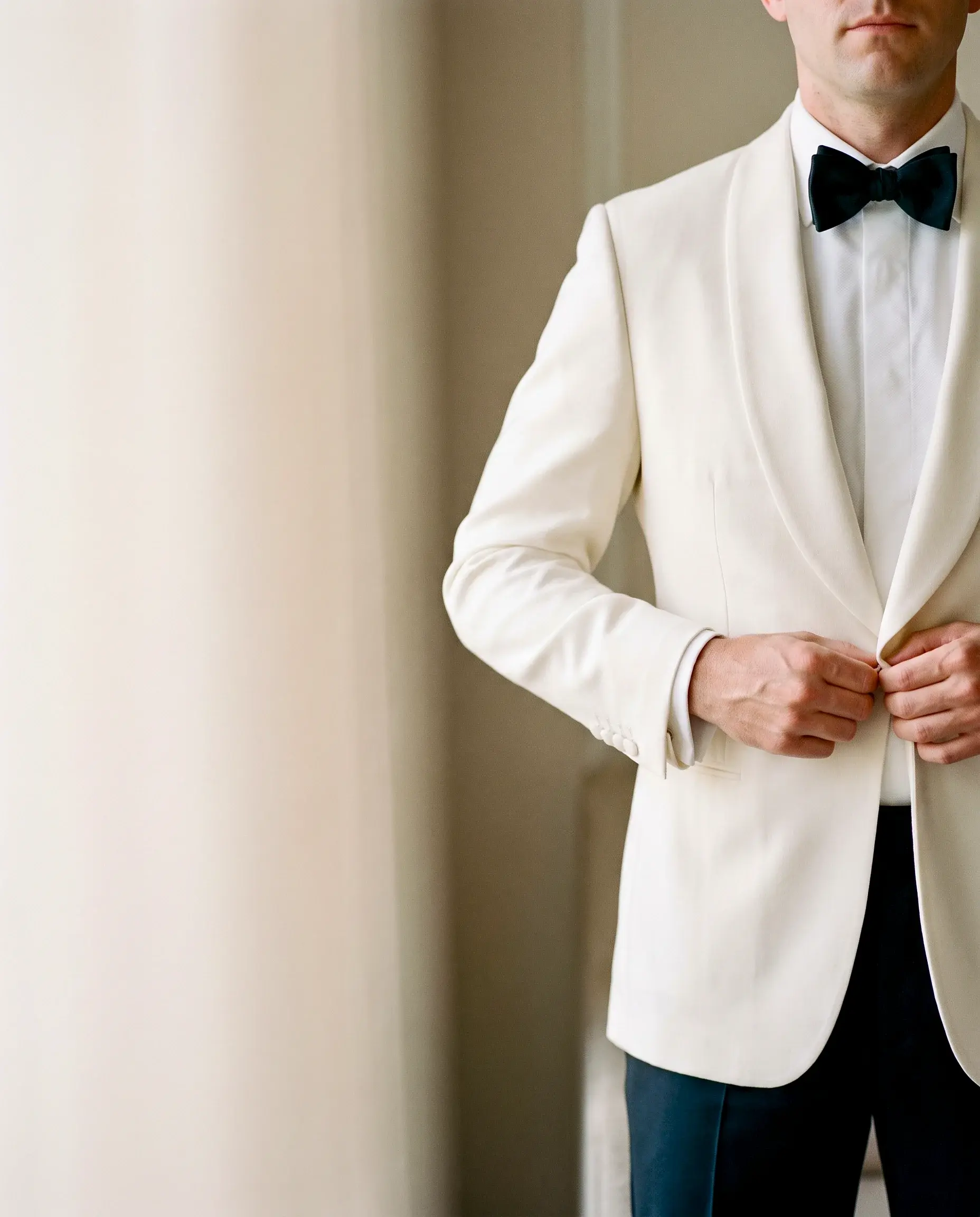 Man in a white dinner jacket and black bow tie buttoning his jacket
