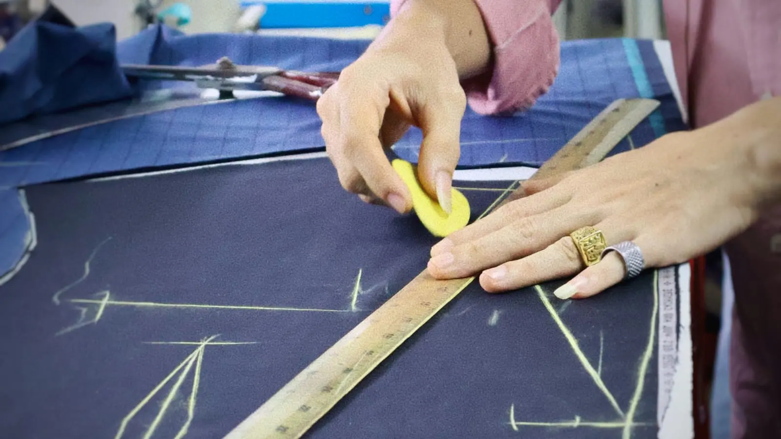 Tailor marking navy cloth with chalk and a wooden ruler before cutting