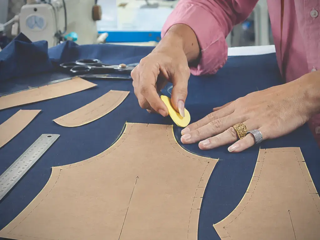 Tailor chalking around paper pattern pieces laid on navy suit cloth
